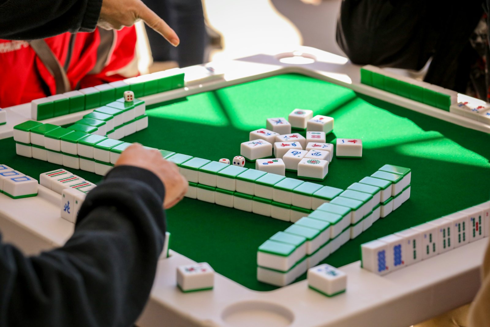 Spelers aan een mahjongtafel met groen laken, stenen en dobbelstenen